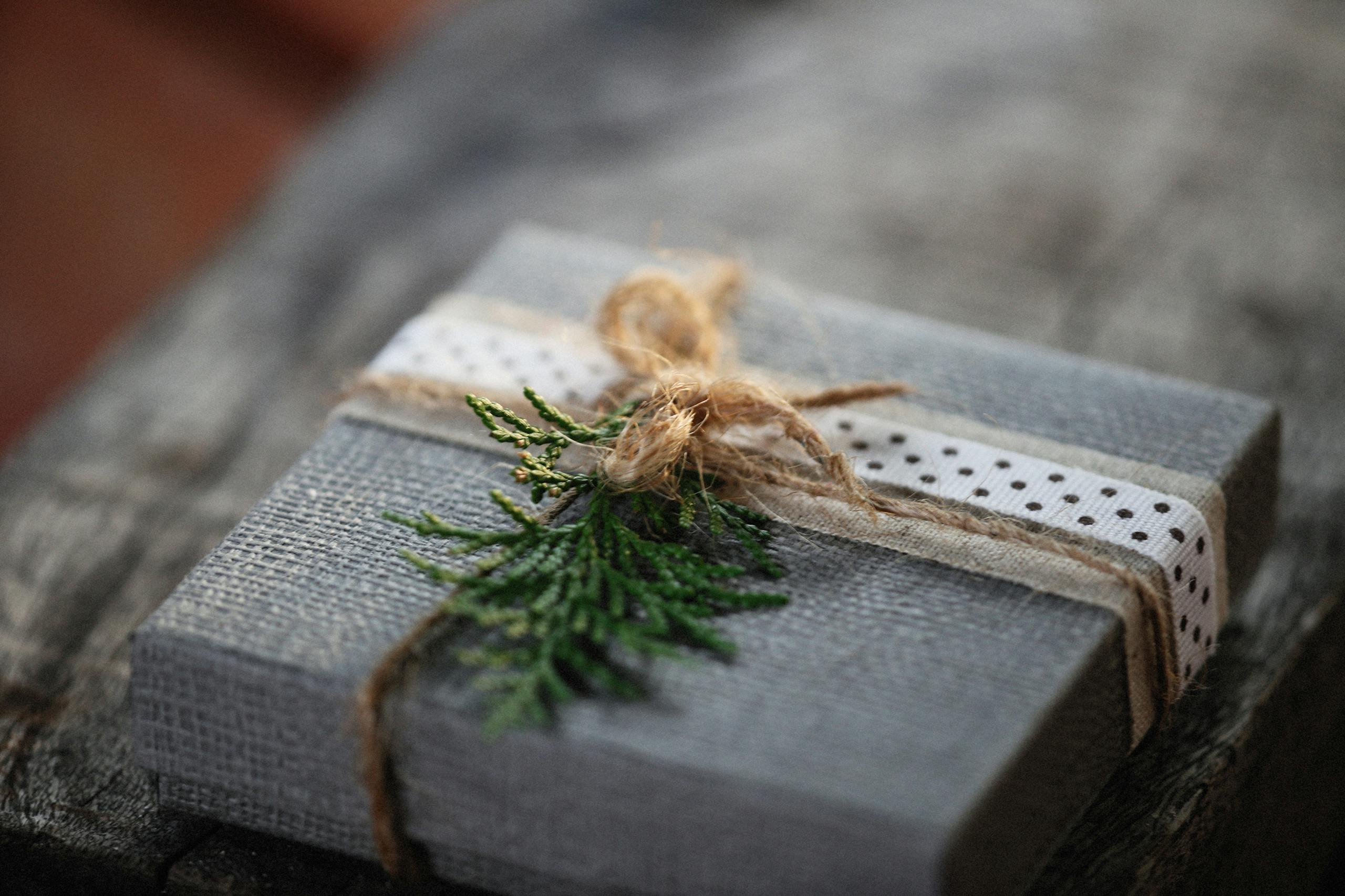 A rustic gift box wrapped with twine and decorated with greenery on a wooden surface.